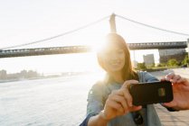 Junge Frau fotografiert sich mit manhattan bridge, brooklyn, usa — Stockfoto