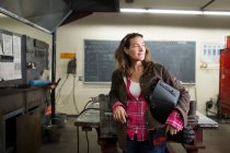 Female metal work teacher leaning against classroom workbench — Stock Photo