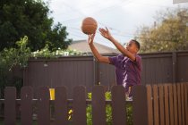 Хлопчик кидає баскетбол біля паркану — стокове фото