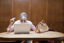 Mujer mayor haciendo compras por Internet usando laptop - foto de stock