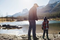 Abuelo y nieto junto al río, vista trasera, Montañas Rocosas, Canmore, Alberta, Canadá - foto de stock