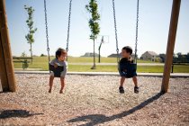 Two boys sitting in swings — Stock Photo