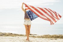 Femme tenant drapeau américain sur la plage — Photo de stock