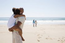 Отец несет дочь на пляже — стоковое фото