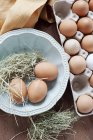 Fresh eggs and straw in bowl, top view — Stock Photo