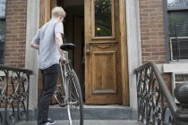 Young man carrying bicycle up steps to front door — Stock Photo