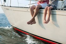 Father and son sitting on yacht, legs dangling — Stock Photo