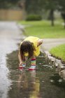 Girl wearing rubber boots picking leaf from rain puddle — Stock Photo