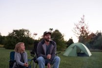 Padre e figlia in campeggio sedie, mangiare marshmallow tostati — Foto stock