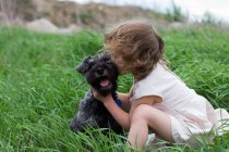 Little girl kissing pet dog on grass field — Stock Photo