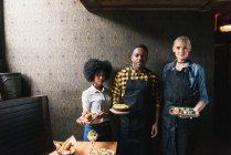 Multikulturelle Freunde blicken in die Kamera und halten Teller mit Lebensmitteln in der Hand — Stockfoto