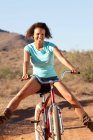 Portrait of young woman cycling downhill in desert — Stock Photo
