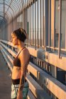 Junge tätowierte Frau läuft auf Brücke mit Sonnenuntergang im Rücken — Stockfoto