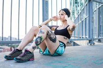 Young tattooed woman doing sit ups on bridge with sunset behind — Stock Photo