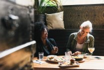 Amigos sonrientes multiculturales compartiendo comida juntos en la cafetería - foto de stock