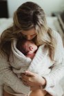Взрослая женщина целует новорожденную дочку, завернутую в кардиган — стоковое фото