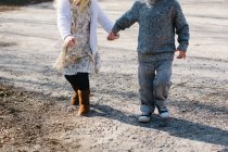 Cropped image of Siblings holding hands walking on gravel road — Stock Photo