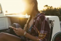 Junge Frau schaut von der Rückseite eines Pickups am Strand von Newport, Kalifornien, USA auf ihr Smartphone — Stockfoto