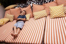 Menino relaxante em móveis listrados ao ar livre com almofadas — Fotografia de Stock