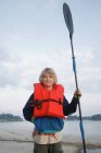 Garçon avec gilet de sauvetage et pagaie de kayak — Photo de stock
