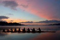 Neuf personnes ramant au coucher du soleil — Photo de stock
