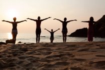 Visão traseira de mulheres praticando ioga na praia ao pôr do sol — Fotografia de Stock