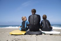 Vue arrière de l'homme et de deux fils assis sur des bodyboards, Laguna Beach, Californie, États-Unis — Photo de stock