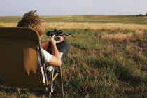 Boy on rural landscape pointing shotgun into distance — Stock Photo