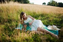 Jeune femme couchée sur le côté dans un champ regardant un appareil portatif — Photo de stock