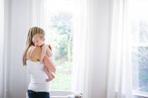 Mid adult woman carrying baby son in living room — Stock Photo