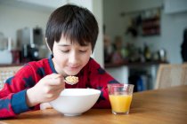 Мальчик ест хлопья на завтрак за столом — стоковое фото