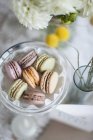Still life of macarons in bowl with flowers in vase — Stock Photo
