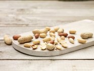 Amendoins inteiros e rachados em tábua de corte de madeira — Fotografia de Stock