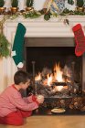 Petit garçon assis près de la cheminée à Noël — Photo de stock