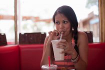 Jovem mulher bebendo milkshake no restaurante, olhando para longe — Fotografia de Stock