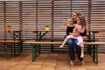 Madre e hija sentadas en el banco en el patio - foto de stock