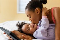 Мати цілує дочку і тримає цифровий планшет — стокове фото