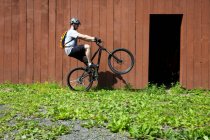 Mountain biker riding on one wheel outside barn — Stock Photo