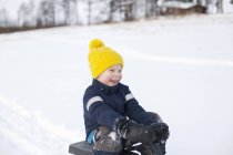 Niño sentado en trineo, en el paisaje cubierto de nieve - foto de stock