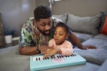 Girl lying on sofa with father playing toy keyboard — Stock Photo