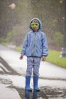 Porträt eines Jungen mit Taucherbrille und Gummistiefeln, der in einer Straßenpfütze steht — Stockfoto