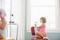 Menina sentada na cadeira por janela comendo gelo alegre — Fotografia de Stock