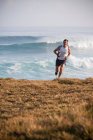 Hombre corriendo en la playa cubierta de hierba - foto de stock