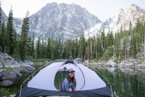 Young woman sitting in tent beside lake, The Enchantments, Alpine Lakes Wilderness, Washington, USA — Stock Photo