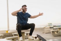 Junger Mann sitzt draußen, benutzt Smartphone und lacht — Stockfoto
