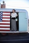 Mulher em pé na porta da caravana com bandeira americana — Fotografia de Stock