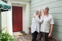 Couple âgé souriant ensemble devant la maison — Photo de stock