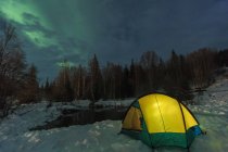 Tent set beside lake under sky illuminated with northern lights — Stock Photo