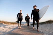Three surfers walking on boardwalk — Stock Photo
