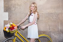 Молода жінка з квітами в кошику велосипеда — стокове фото